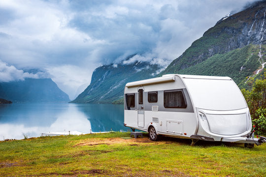 Modern caravan parked in a natural setting with privacy screen, cover, and accessories set up for camping.